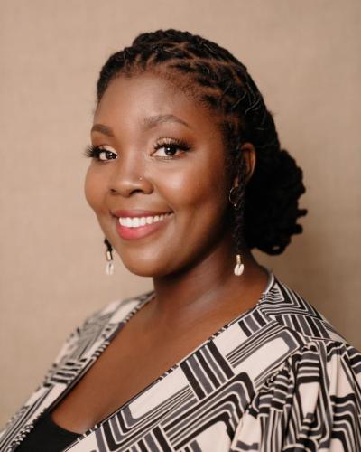 A woman smiles while looking off to the left, wearing a black and white patterned top and dangling earrings.