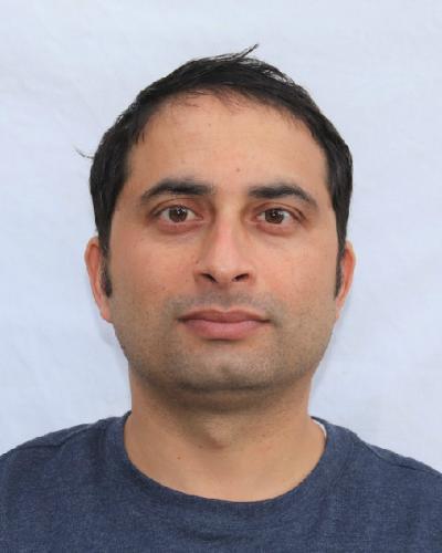 A man with dark hair and a blue shirt looks at the camera.