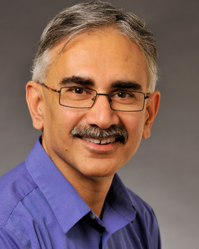 A man wearing glasses and a blue shirt smiles at the camera.