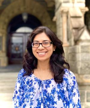 shenila khoja-moolji outside, she has shoulder length dark hair and wears glasses and a blue and white floral blouse